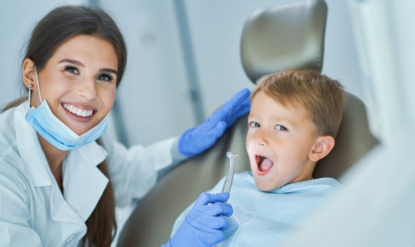 Toddler smiling during first dentist visit with parent and pediatric dentist